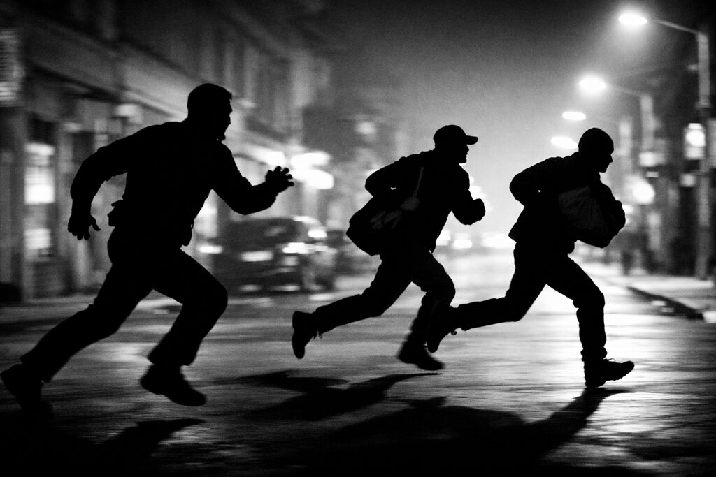 Tre figure in fuga nella notte lungo una strada cittadina